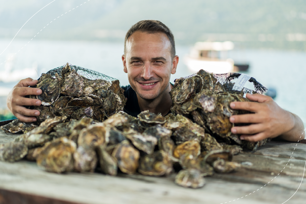 A man proudly holds a cluster of fresh oysters in his hands, highlighting their rough shells and the freshness of the seafood.