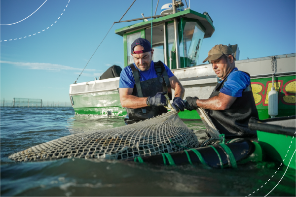 Two fishers standing in the sea holding net. Their boat is visible behind them.